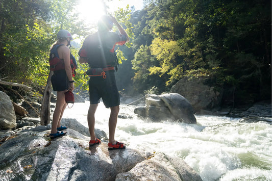 Two raft guides scouting rapids on the Chattooga River wearing Astral PFD Sandal Fire Orange and Webber Water Blue